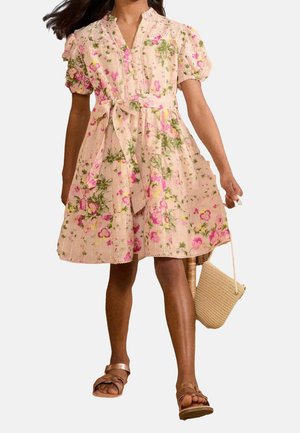 Bloemenjurk van lichtroze stof met pofmouwen, getailleerde taille en ceintuur met strik. Voorzien van groene en roze bloemen; gecombineerd met een geweven tas.