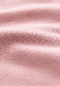 Minkšta rožinė medvilnės audinio tekstūra, turinti subtilius raštus ir raukšles, kurios suteikia gilumą ir judesį.