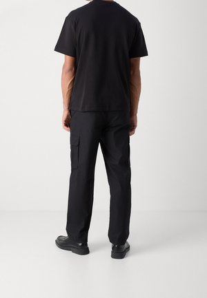 Černé bavlněné tričko s krátkými rukávy, doplněné černými cargo kalhotami s bočními kapsami a rovného střihu, doplněné černými botami.