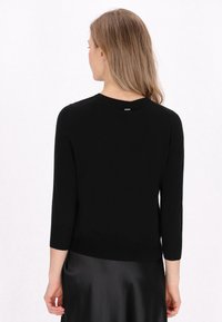 Maglione nero di lunghezza media con collo rotondo e maniche a tre quarti. Realizzato in un tessuto morbido, presenta un piccolo logo sulla parte posteriore.