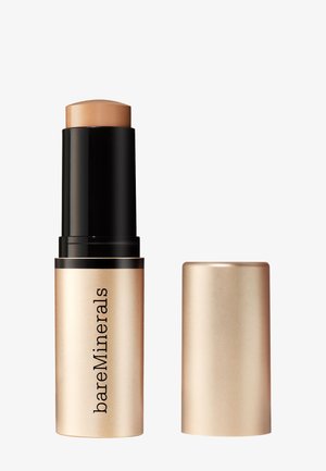 Stick de fond de teint BareMinerals en teinte beige avec base noire à remonter et capuchon beige assorti posés à côté sur fond blanc.