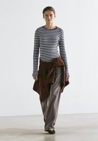 Striped long-sleeve top in blue and brown, paired with loose brown pants and a tied rust-brown sweater. Simple flats complete the outfit.