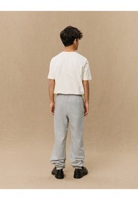Kurzärmliges cremefarbenes T-Shirt, graue Sweatpants und schwarze Schuhe. Die Sweatpants haben elastische Bündchen, eine weiche Textur und eine lässige Passform.