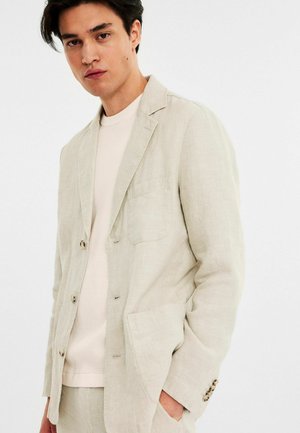 Linning blazer i ljusbeige med en ficka, slagkrage och tre knappar. Bärs över en ljus stickad topp med texturerad tyg.