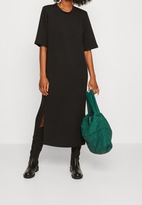 Schwarzes Midi-Kleid mit kurzen Ärmeln, seitlichen Schlitzen und rundem Ausschnitt. Kombiniert mit knielangen schwarzen Stiefeln und einer grünen gesteppte Tasche.
