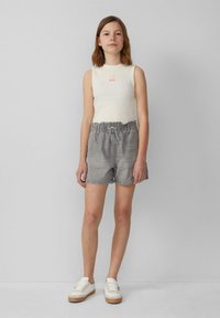 Kremowy bezrękawnik z małą grafiką, zestawiony z szarymi szortami dżinsowymi z elastycznym paskiem. Białe sneakersy z beżową podeszwą.