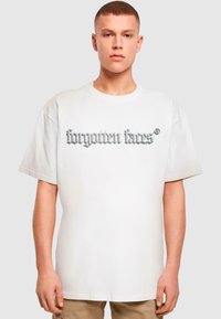 Weißes Baumwoll-T-Shirt mit großem grauem gotischen Text "forgotten fans®" auf der Vorderseite; legerer Schnitt mit kurzen Ärmeln und Rundhalsausschnitt.