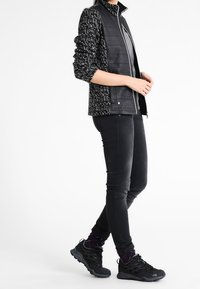 Svartvitt mönstrad jacka med hög krage, kombinerad med svarta slim fit-jeans och svarta sportskor.