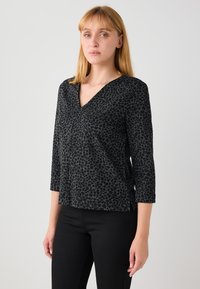 Haut noir à col en V avec un motif léopard texturé, manches trois-quarts et fentes latérales, associé à un pantalon noir.
