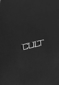 Superficie in pelle nera con un logo metallico argento che legge "CULT", che mostra un design moderno e minimalista. Texture liscia senza motivi visibili.