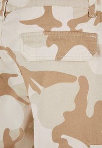 Beige camo-patterned fabric features smooth texture and a small, rectangular back pocket with a stitched outline.