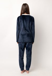 Conjunto de ropa de lounge de forro polar azul marino con mangas largas y pantalones. Textura suave, puños en las muñecas y tobillos, y un detalle de cuello blanco.