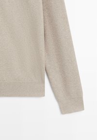 Maglione beige lavorato a maglia con trama testurizzata, dotato di scollo rotondo e polsini e orlo a coste. Presenta accenti di fibre chiare sfumate.