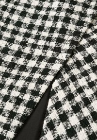 Tessuto testurizzato in bianco e nero con motivo a quadri gingham, ripiegato per rivelare un rivestimento nero uniforme sottostante.