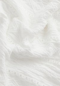 Tissu blanc texturé présentant des motifs en relief et des détails découpés, avec une apparence douce et tissée. Convient à divers usages textiles.
