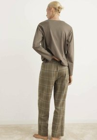 Langsleeve, olijfgroen top en geruite, hooggetailleerde broek in aardetinten met blauwe accenten. Zacht materiaal getoond vanuit een achteraanzicht.