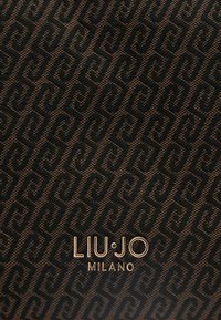 Schwarz gemustertes Textil mit einem stilisierten Wirbelmuster und einem goldenen "LIU·JO MILANO" Logo, das unten deutlich sichtbar ist.