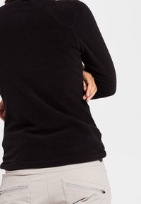 Mustat fleece-paita pyöreällä kaula-aukolla, sileällä pinnalla ja pitkillä hihoilla. Sisältää huomaamattomat saumat hartioissa ja tiukan istuvuuden.