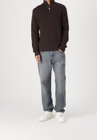 Hnědý texturovaný pletený svetr s límcem na čtvrtinu, zkombinovaný se světle modrými volnými džíny a bílými teniskami.