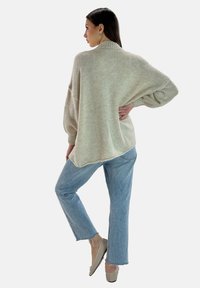 Ljusbeige oversized tröja med hög hals och ribbstrukturen, ihopparad med ljusblå raka jeans och beiga skor.