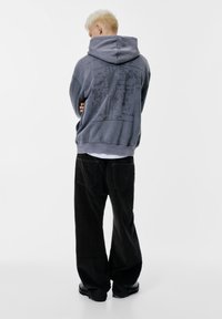 Hanorac gri supradimensionat cu un design texturat pe spate, asortat cu pantaloni largi din catifea căptușită negri și cizme negre.