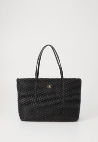 Svart vevd tote bag med teksturert overflate, med forlengede svarte håndtak og en gull "CK"-logo midt foran.