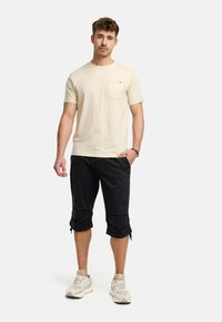 Beige bomull t-skjorte med brystlomme, kombinert med svarte cropped bukser med justerbare kanter og innsnøring. Nøytrale sneakers.