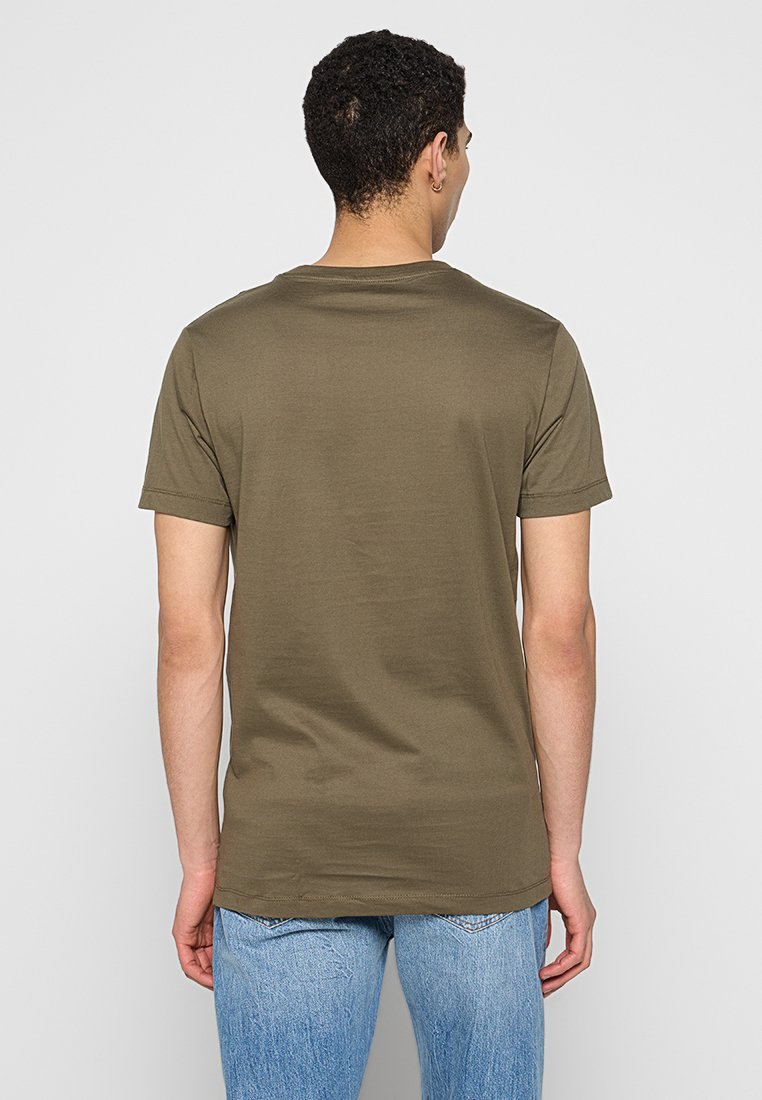 Olivgrünes Baumwoll-T-Shirt mit kurzen Ärmeln, Rundhalsausschnitt und weicher Textur, von hinten betrachtet, kombiniert mit hellblauen Jeans.