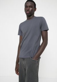Tricou din bumbac gri, cu guler rotund și mâneci scurte, asortat cu blugi gri închis, lejeri. Textură netedă, design minimalist.