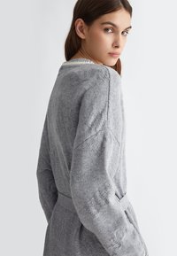 Maglione grigio a maglia con un motivo testurizzato, maniche ampie e una cintura coordinata. Presenta un colletto a coste e un tessuto morbido e caldo.