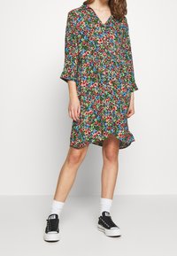 Blommig klänning med korta ärmar, V-ringning och volangärmskant; har en livlig blandning av röda, blå och gröna blommor på en mörk bakgrund.