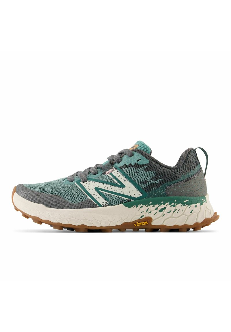 Trailrunning-Schuh mit einem strukturierten Obermaterial aus grünem und grauem Mesh, weißer Zwischensohle, braunem Gummiaußensohle und auffälligem Vibram-Logo.