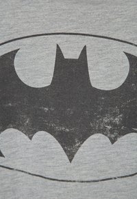 Szara bawełniana koszulka z dużym czarnym logo Batmana, gładka faktura, z wyblakłymi detalami i okrągłym obramowaniem wokół emblematu.