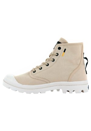 Zapatilla alta de color beige hecha de lona con ojales negros, puntera redonda de goma blanca, suela texturizada blanca y una lengüeta negra en el talón.