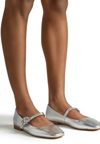 Zilveren metallic platte schoenen met een spitse neus, voorzien van een smalle band en versierde bloemdetails aan de zijkant. Gladde textuur.