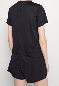 Svart idrottströja med korta ärmar, slät textur, rundad nederkant och platta sömmar, matchad med svarta shorts.