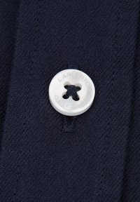 Granatowa dzianina z dużym białym guzikiem z czterema otworami i wytłoczonym logo marki. Widoczne szwy wokół guzika.