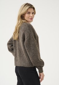 Pulover maro, pufoș cu tiv și manșete ripsate. Are un croi lejer și umeri căzuți. Asortat cu pantaloni negri.