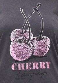 Svart T-skjorte med grafikk av tre rosa kirsebær med teksturert design. Ordet "CHERRY" er trykt i fete rosa bokstaver nedenfor.
