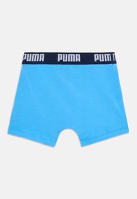 Felgroene boxershorts met een marineblauwe tailleband waarop herhaaldelijk witte PUMA-logo's staan, plat op een witte achtergrond gelegd.