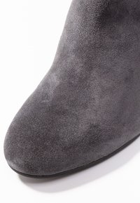 Bottine en suède gris avec un bout pointu et une texture lisse. La semelle est noire et la hauteur est typique d'un design à talon moyen.