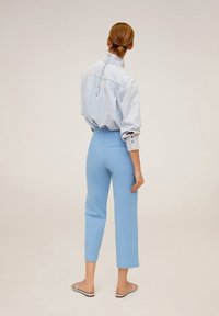 Pantalons ajustés bleu clair à taille mi-haute, associés à une chemise en denim clair ample avec fermeture à boutons et manches retroussées.