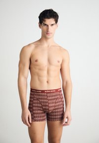 Red and brown patterned boxer shorts featuring a branded elastic waistband. The design includes a repetitive geometric print.
