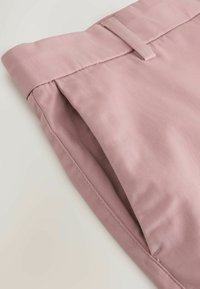 Gros plan sur la ceinture et la poche latérale d'un pantalon rose clair, mettant en évidence le passants de ceinture et la texture du tissu.