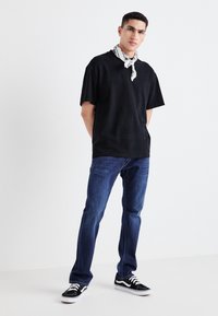 Svart kortärmad t-shirt, lös passform, i kombination med blå denimjeans. Svart och vit mönstrad scarf knuten runt halsen, svarta sneakers.