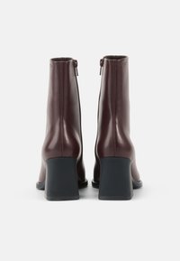 Maroon leather ankle boots with a sleek design, featuring a high block heel and a rear zipper for easy wear. Smooth texture, minimalist style.