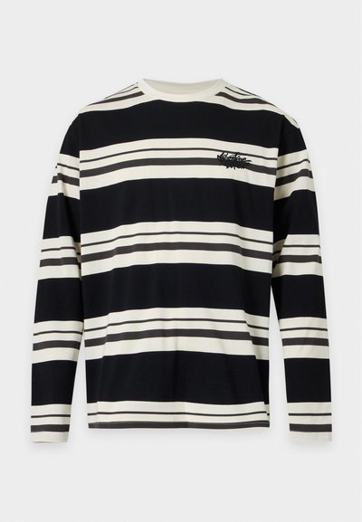 T-shirt à manches longues avec col rond, larges rayures horizontales noires et blanches, et petit logo noir brodé sur la poitrine gauche.