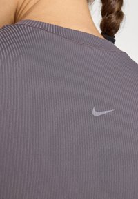 Hallhalli triiksärk hallist ripsmetest, millel on peegeldav Nike'i logo. Kujundusel on ümar kaelus ja pehme, tekstureeritud kangas.