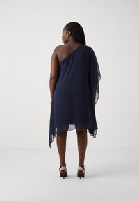 Robe en chiffon bleu marine à une épaule avec un ourlet asymétrique et une superposition transparente. Présente une silhouette fluide et un détail au dos.