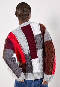 Sweter dzianinowy w wzór patchworkowy z różnymi odcieniami: czerwonym, szarym, białym, bordowym i brązowym. Teksturowane wzory warkoczy na całej powierzchni.